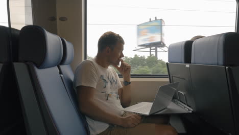 Vista-De-Un-Joven-Viajando-En-El-Tren-Y-Trabajando-Con-Una-Computadora-Portátil-En-La-Mesa-Contra-La-Ventana-Países-Bajos