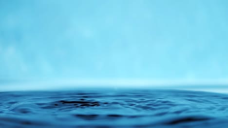 slow motion 4k video of a water surface with falling drops on a blue background. splashing water. studio shooting.