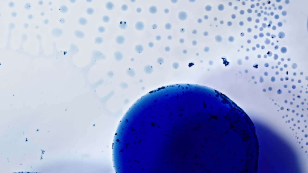 Blue alcohol ink spreads in macro shot, forming abstract dots and soft gradients