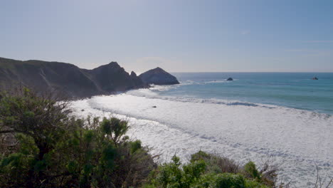 hillside view of the pacific ocean with rolling waves crashing along the shore on a sunny day of big sur california