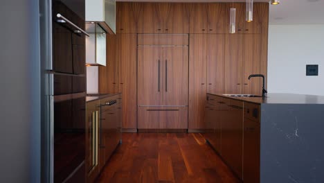 Wide-shot-of-modern-kitchen-with-black-countertops-and-appliances,-with-grand-dark-wood-cabinets