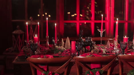 beautifully decorated table for festive christmas dinner. burning candles, pine cones, figurines and luxurious crockery in the room lit in red color.