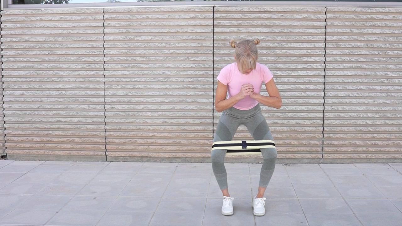 Una donna fa squat con fascia di resistenza all'aperto in abbigliamento sportivo per sviluppare la forza delle gambe.