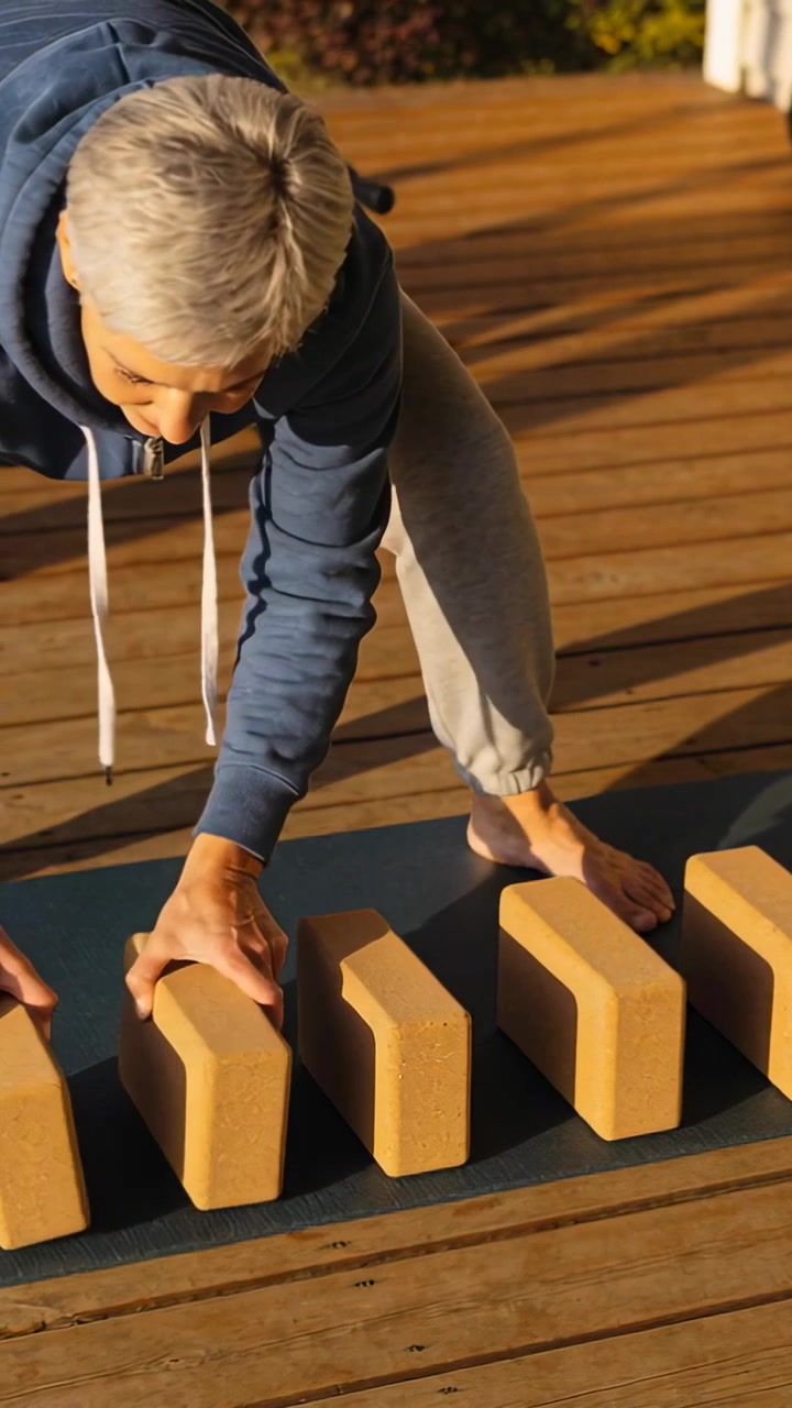 Vertical video: Prepping hooded senior placing cork yoga blocks on mat on sunlit deck for workout