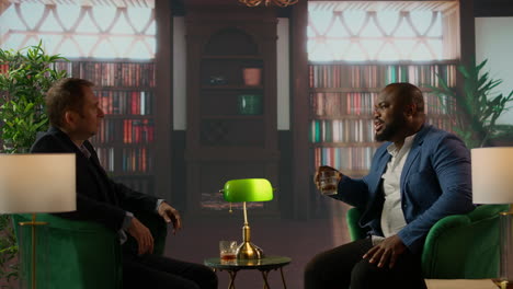 two multiethnic businessmen sharing a whiskey glass in an elegant library