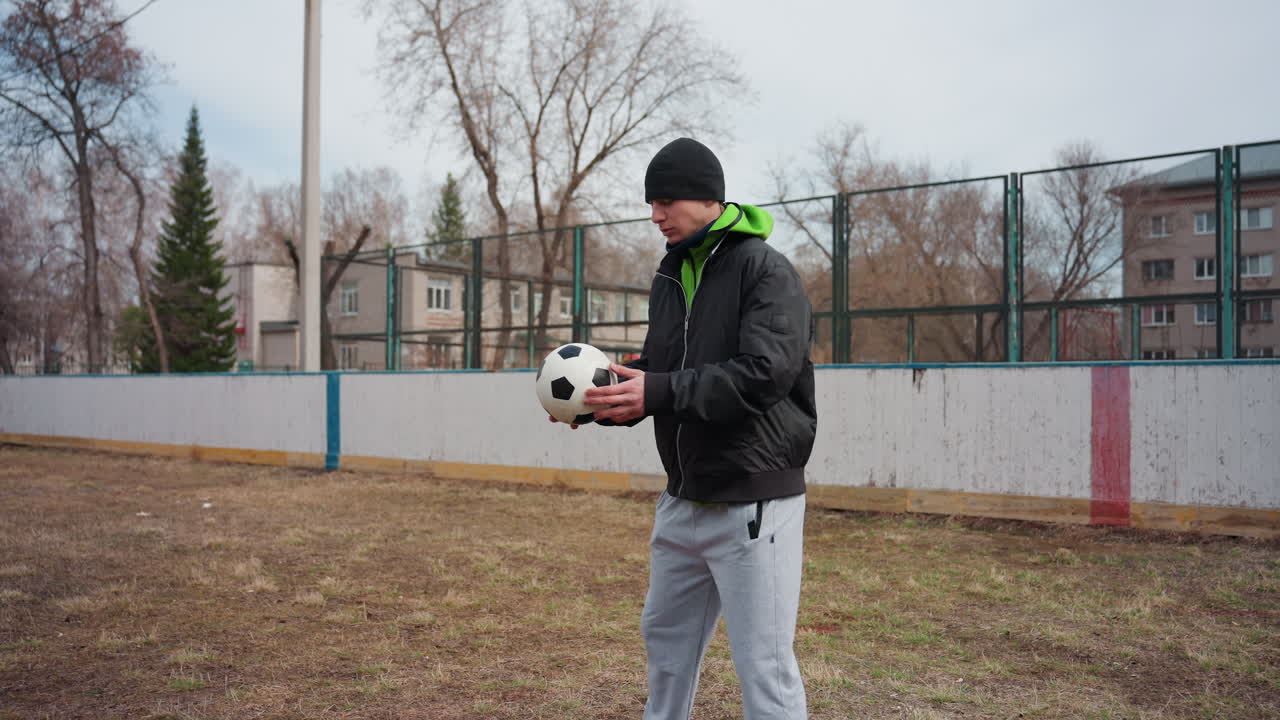 Un portero urbano practica con un balón de fútbol; entrenamiento de habilidades futbolísticas en un entorno urbano frío; un atleta masculino practica ejercicios de equilibrio y fuerza con un balón de fútbol en un entorno urbano.