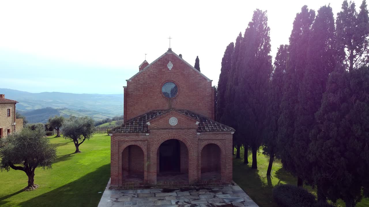 drone footage of Montecucco, Tuscany, the camera stays facing the church as it pulls back slowly, vineyards surrounding the historic building.
