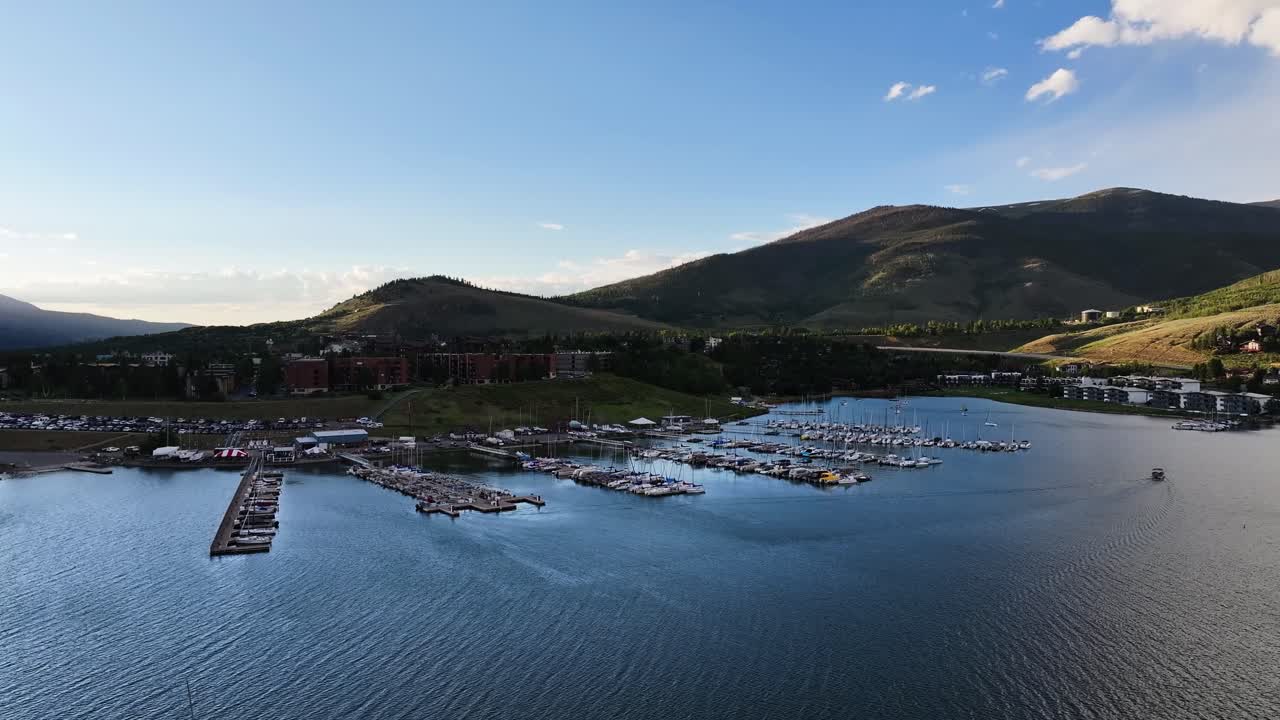 Dillon Dam reservior in Silverthorne Colorado Marina and sailboats at sunset orange light hitting the mountains AERIAL TRUCKING PAN