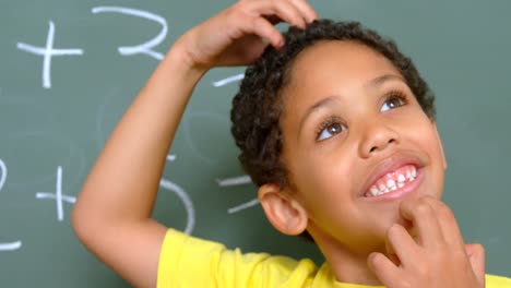 Front-view-of-thoughtful-African-American-schoolboy-and-standing-against-chalkboard-in-classroom-4k