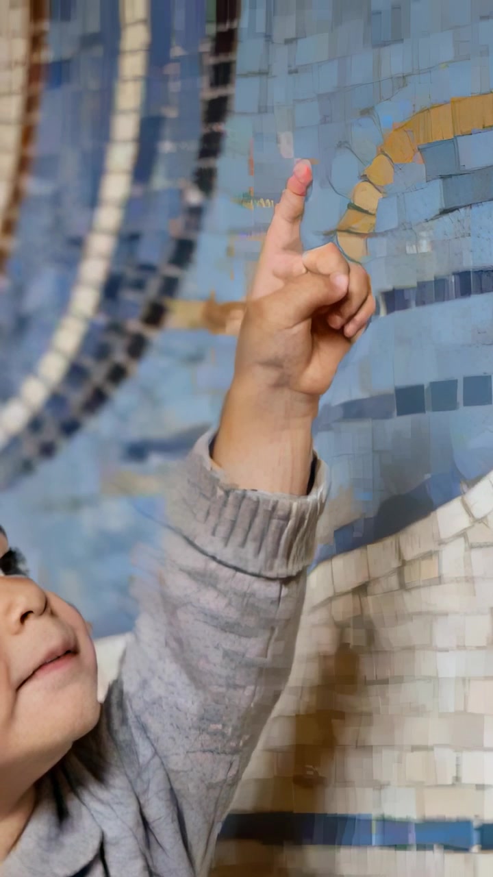 Video vertical: Viendo un mosaico, niño levantando el dedo derecho en una pared de azulejos con suéter gris, espacio para texto.
