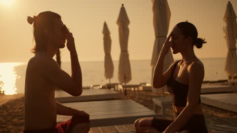 a brunette girl and a brunette guy in beachwear are doing meditation and doing yoga and breath of fire. yoga class on sunny