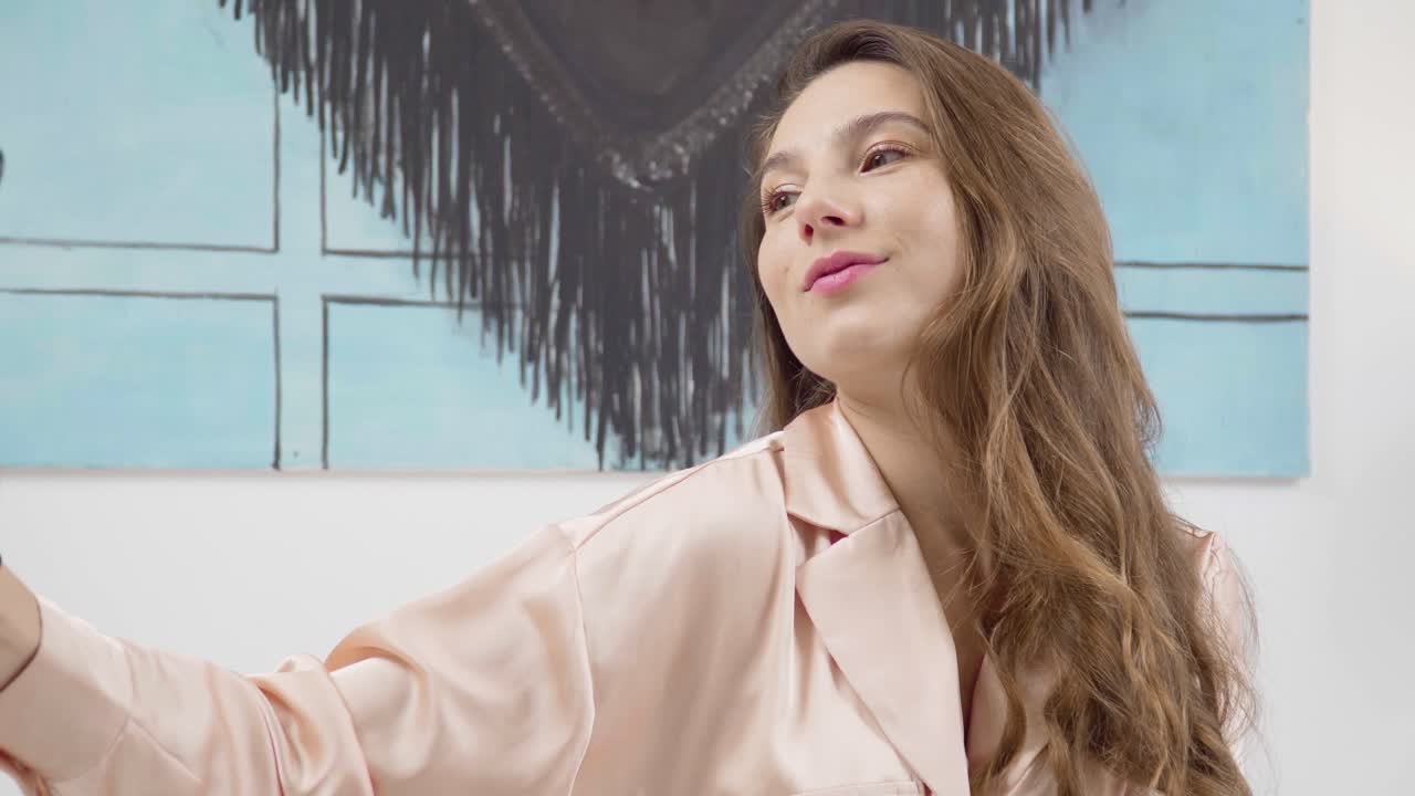 Portrait of a cute cheerful woman in pink pajamas in the bedroom taking silly selfies