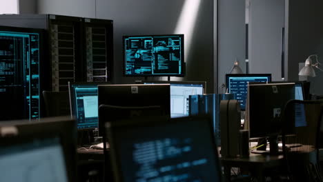 a server room or data center with multiple computer monitors displaying code and data, featuring a partially visible person