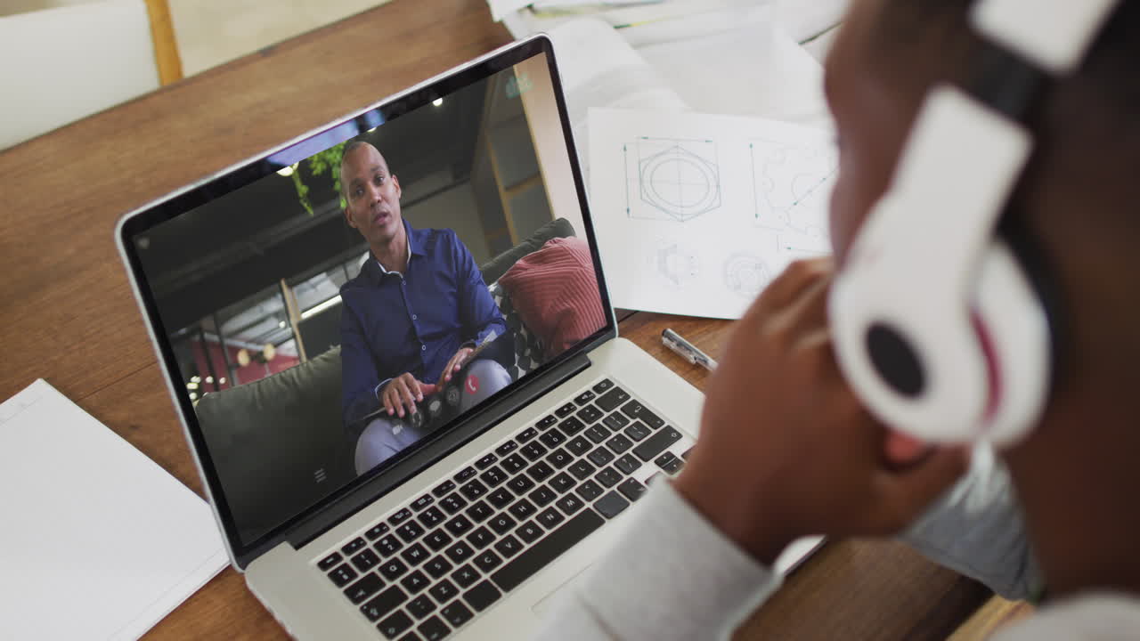 African american businessman sitting at desk using laptop having video call with male colleague