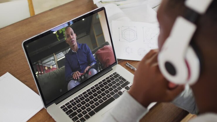 African american businessman sitting at desk using laptop having video call with male colleague