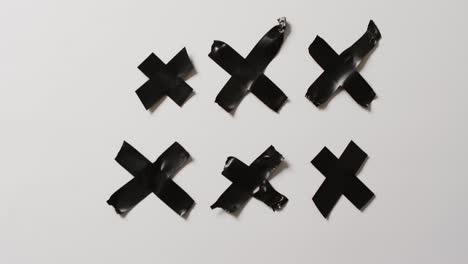 Video-of-close-up-of-black-tape-forming-crosses-on-white-background