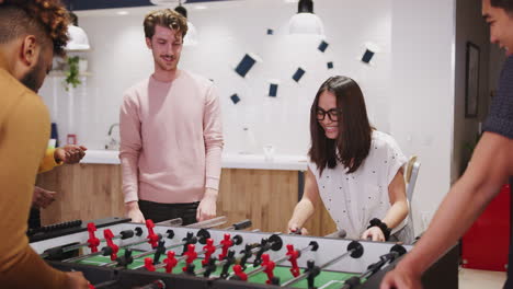 young business creatives playing table football together at work celebrate a goal, close up