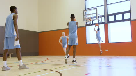 Basketball players practicing dribbling and shooting in bright indoor court