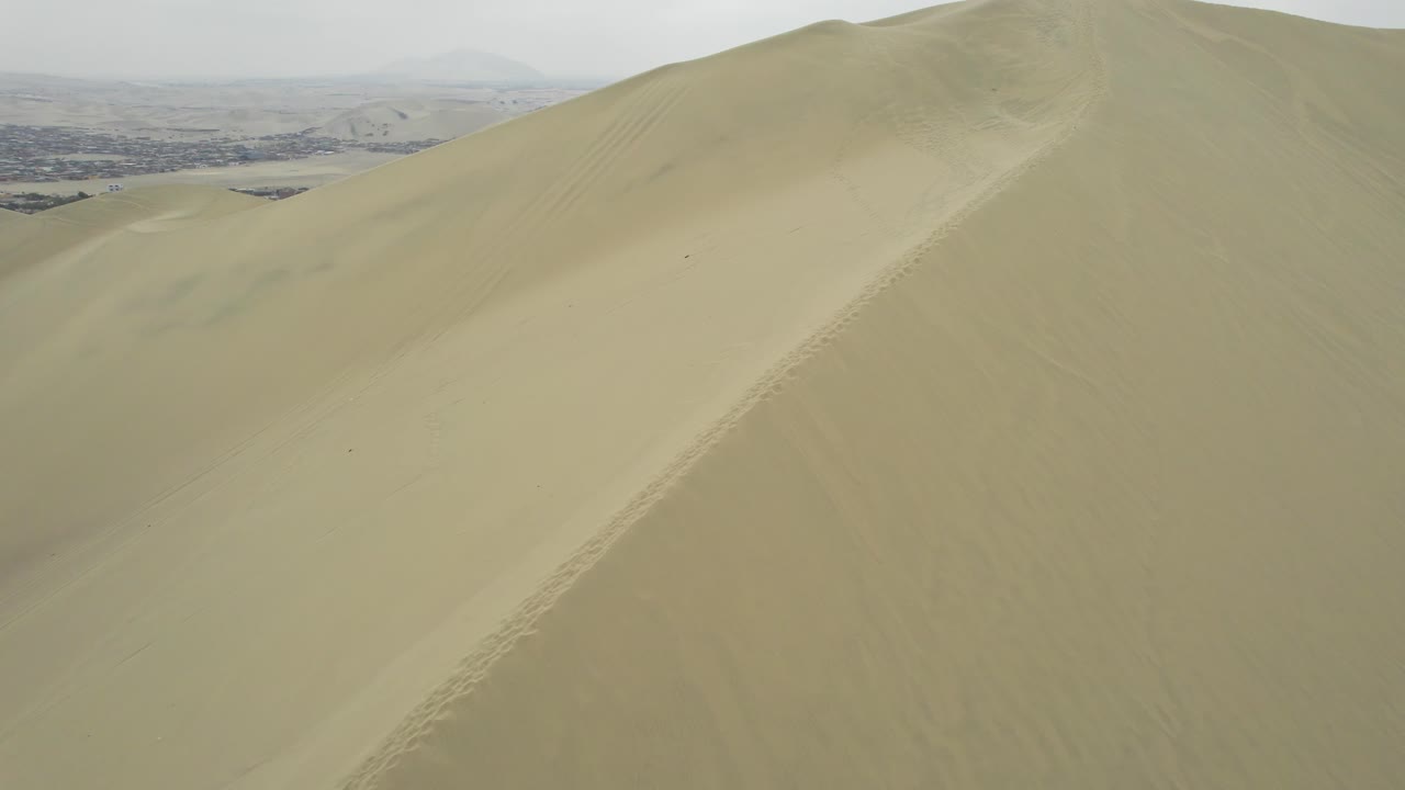 Vista aerea di persone che camminano su una grande duna di sabbia con una città in lontananza