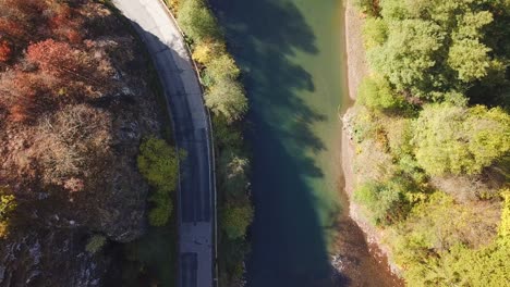 forward drone shot, top view, of a river flowing surrounded by autumn trees, next to a country road