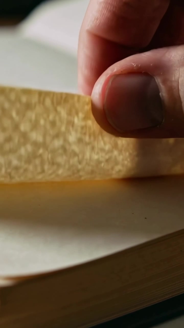 Vertical video: Fingertips lifting, adult hand turning textured book page on desk for reading