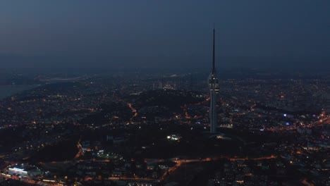 wide view of huge new tv tower of istanbul with mosque on hill in background at night, aerial drone shot