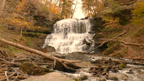 a cascading waterfall in a wooded area with orange and brown tones