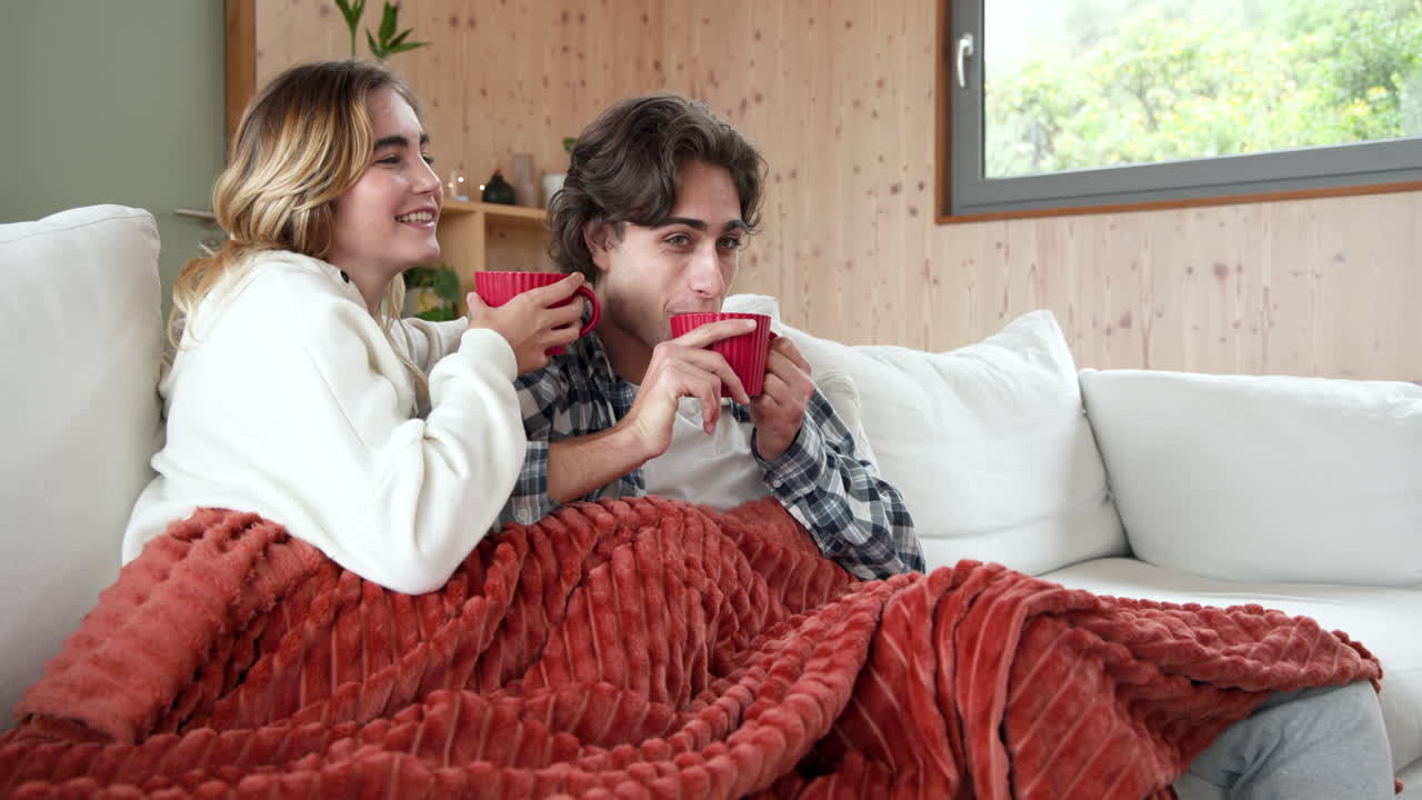 Juletid, par nyder varme drikke på hyggelig sofa derhjemme, pakket ind i tæppe, kopiplads.