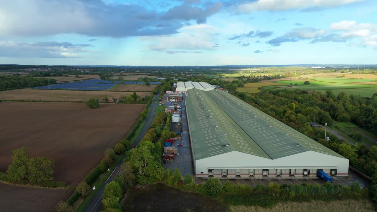 Aerial drone view of industrial warehouse in rural landscape with solar power plant photovoltaic energy, UK Europe
