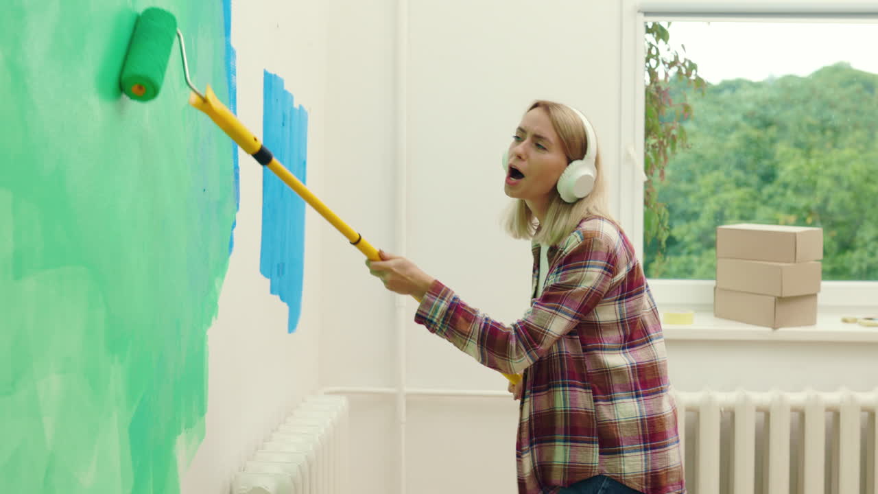 Woman painting a wall with a roller while listening to music