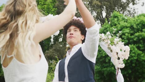 Happy-diverse-couple-dancing-in-garden-on-sunny-day-at-wedding