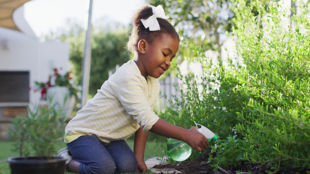 feliz niña afroamericana jardinería, regar las plantas en el jardín