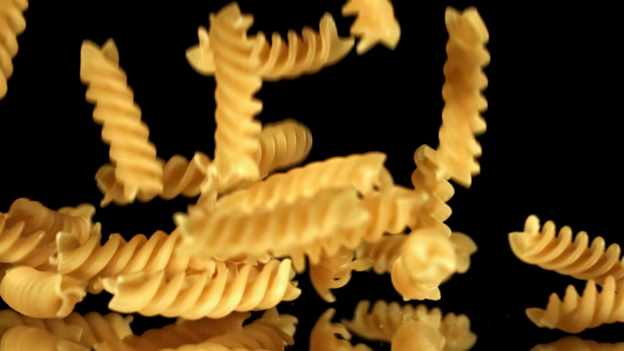 Fusilli che cadono al rallentatore su sfondo nero.