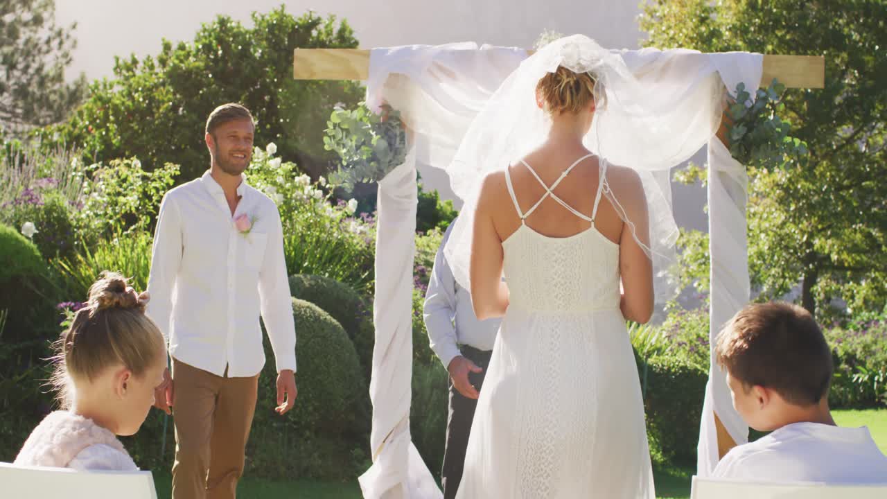 Caucasian bride walking to outdoor altar to groom and wedding officiant