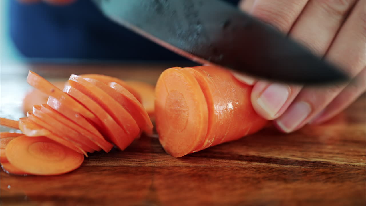 Close up of a woman cutting up a carrot on a wooden cutting board