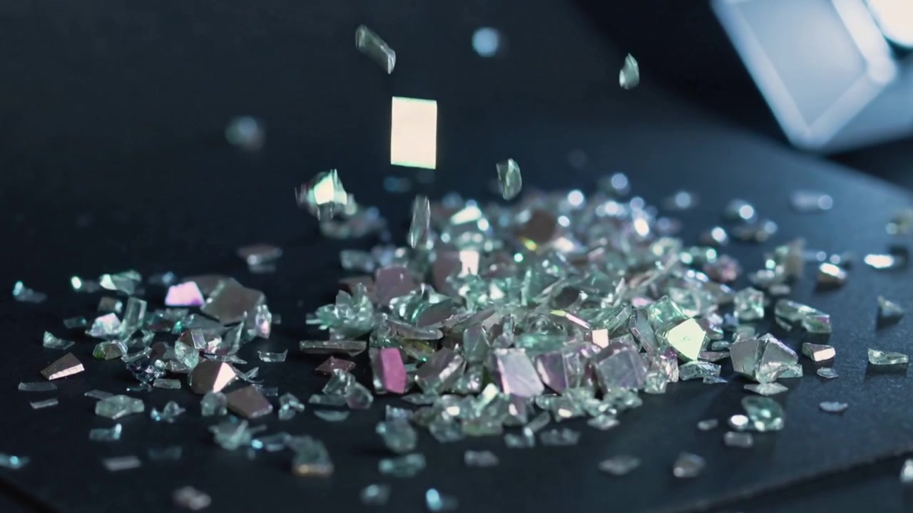 Chute d'éclats de verre facettés heurtant une table sombre, formant un tas étincelant sous une lumière LED vive.