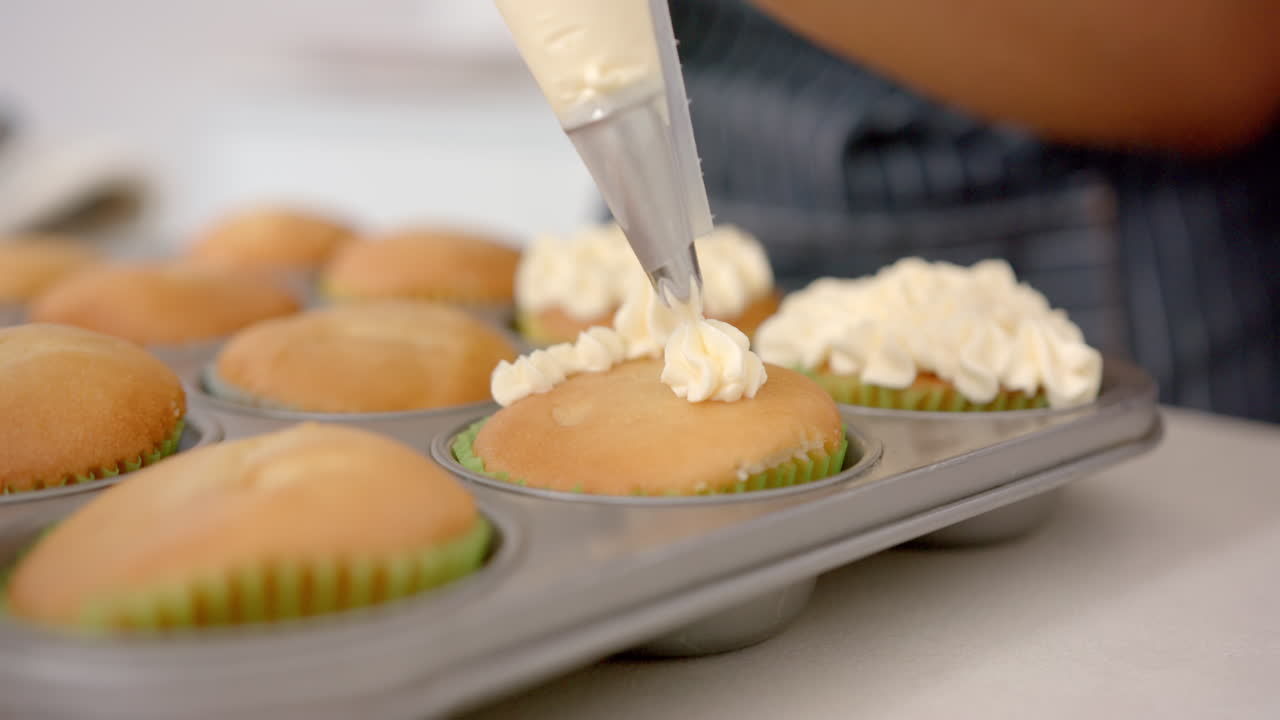 Decorating cupcakes with frosting, person using piping bag in kitchen
