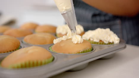 decorating cupcakes with frosting, person using piping bag in kitchen