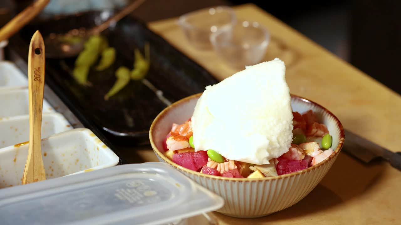 Bidikan close-up statis tangan yang meletakkan busa putih di atas semangkuk poke bowl Jepang yang segar