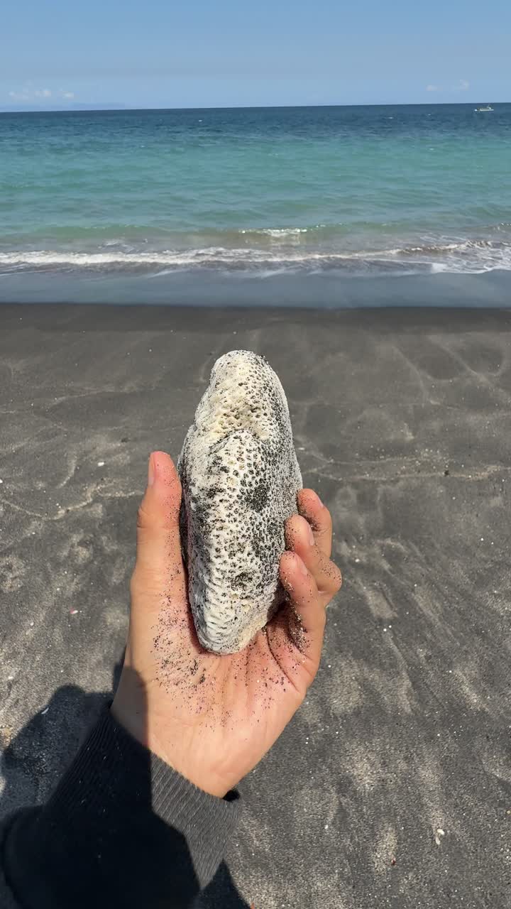 Mano che tiene corallo bianco su una spiaggia di sabbia nera con onde dell'oceano