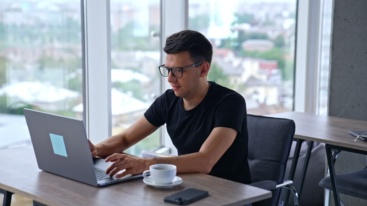 Young productive resilient man working at laptop in office. Male freelancer looking intently at the screen and typing something. Close up.
