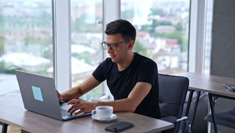 young productive resilient man working at laptop in office. male freelancer looking intently at the screen and typing something. close up.