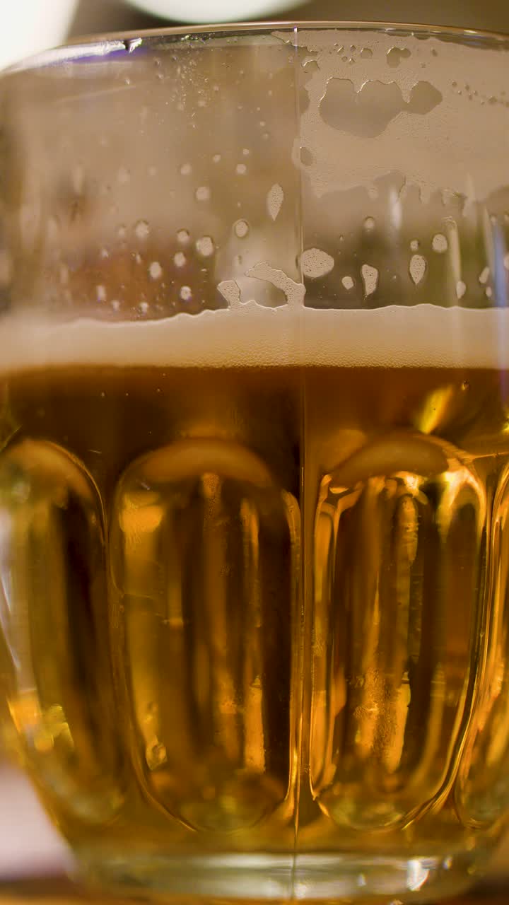 Boccale di vetro di birra lager dorata con schiuma, primo piano, ripresa statica, illuminazione interna calda