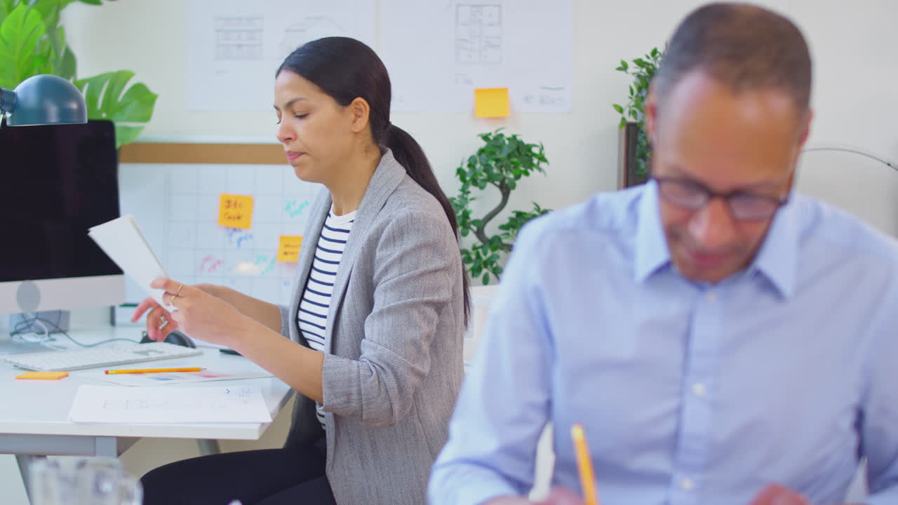 남성과 여성 건축가들이 사무실에서 새로운 건물의 계획을 작성하는 데 책상에 앉아 있습니다.
