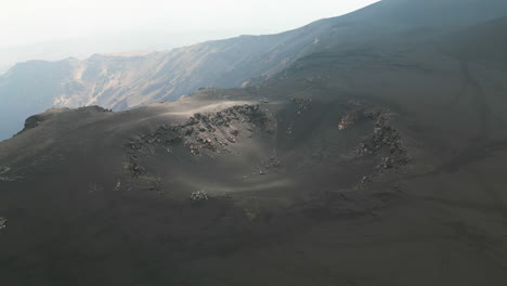 break in cloud shadow casts light across dark basalt black soil in crater of etna volcano