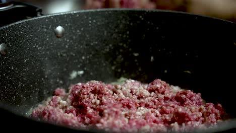 a close-up of a hand placing minced beef into a cooking pot on the stove.