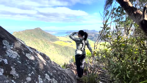 Dark-haired-woman-overlooks-wide-mountain-view-after-a-windy-hike-in-new-zealand