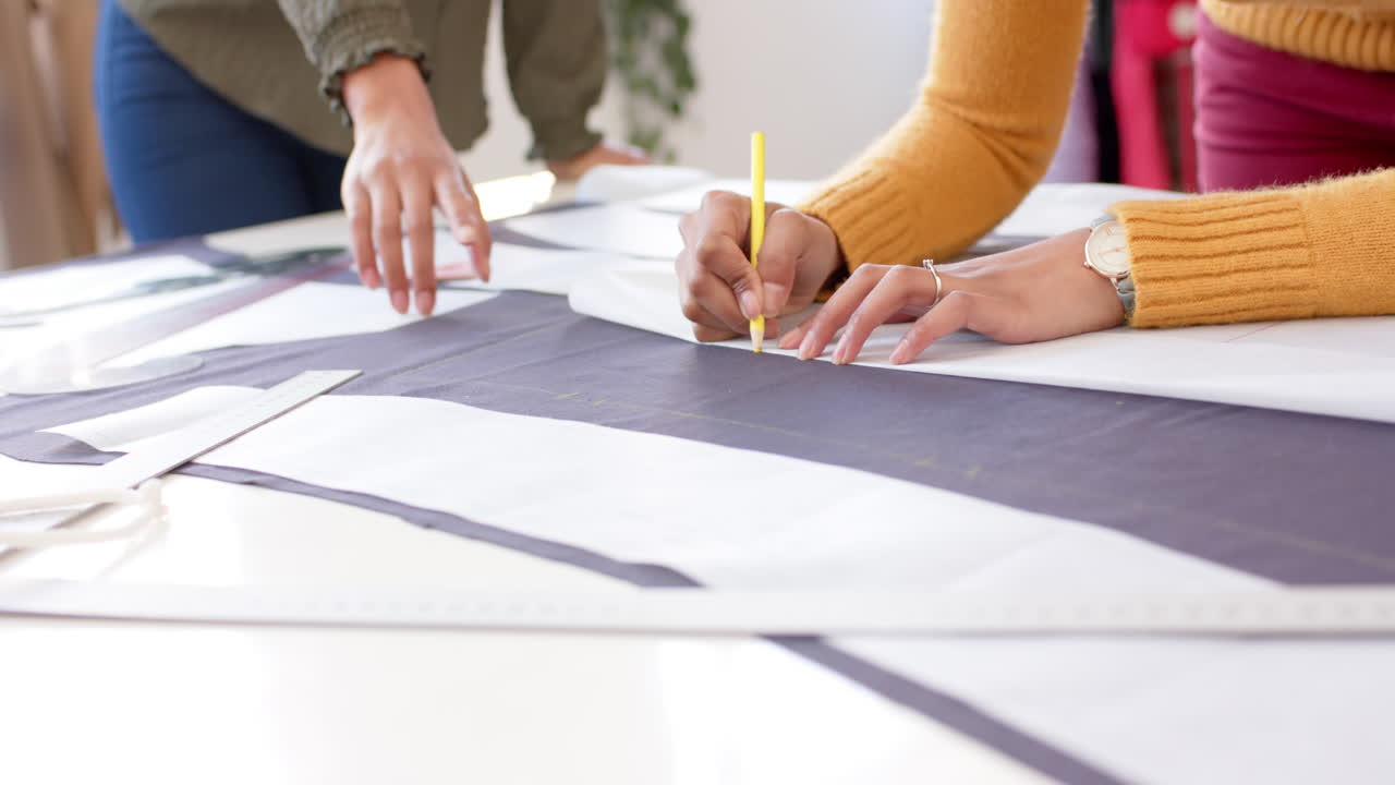 Diverse female fashion designers marking pieces of cloth from design patterns on table, slow motion