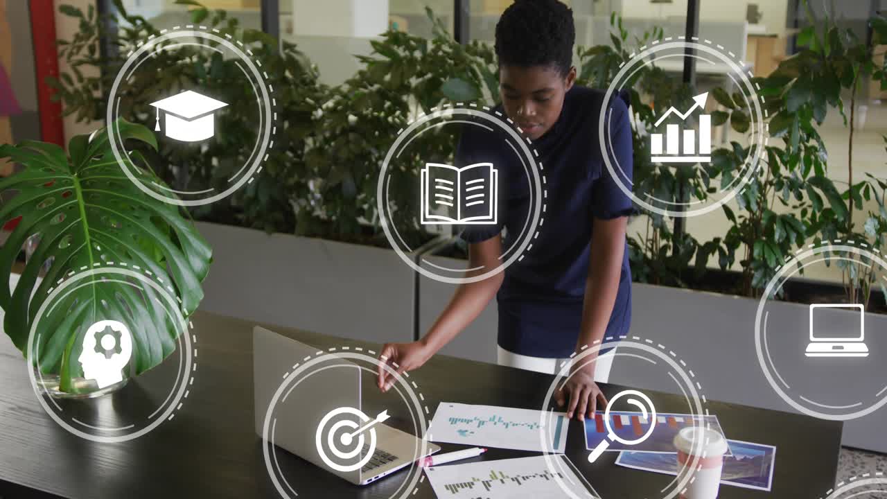 Female worker approaching table, touching laptop, activating icons while reviewing business charts