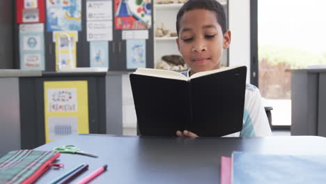 En-Un-Ambiente-Escolar,-Un-Joven-Estudiante-Afroamericano-Está-Absorto-En-La-Lectura-En-Un-Salón-De-Clases